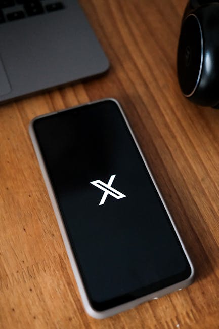 pexels-photo-19826630-19826630 Smartphone displaying a logo on a wooden desk next to a laptop and headphones.